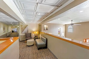 Corredor de hotel com mesa de recepção, área de estar e ventilador de teto.