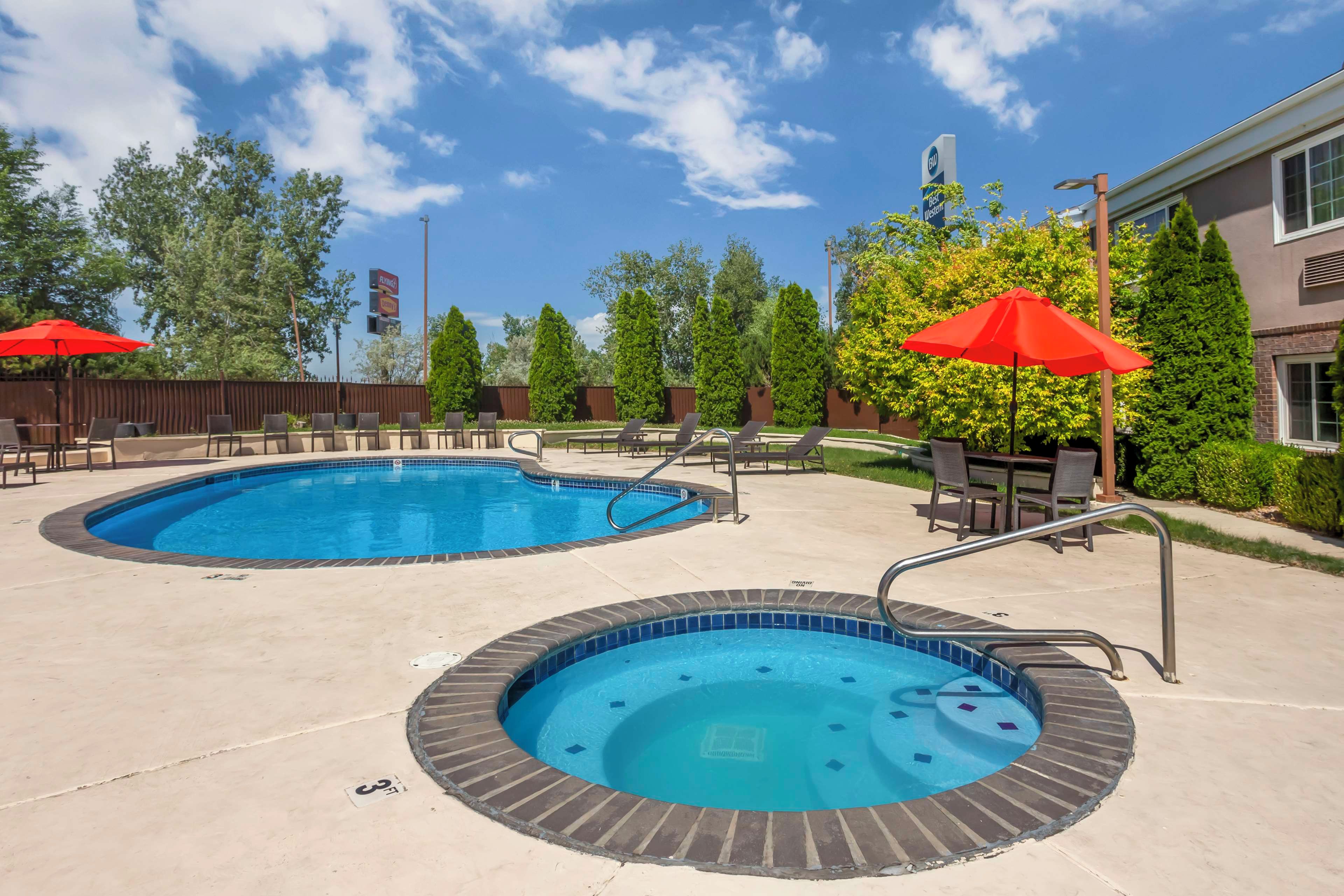 A pool area with two hot tubs and lounge chairs, surrounded by trees and a building.
