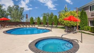 A pool area with two hot tubs and lounge chairs, surrounded by trees and a building.