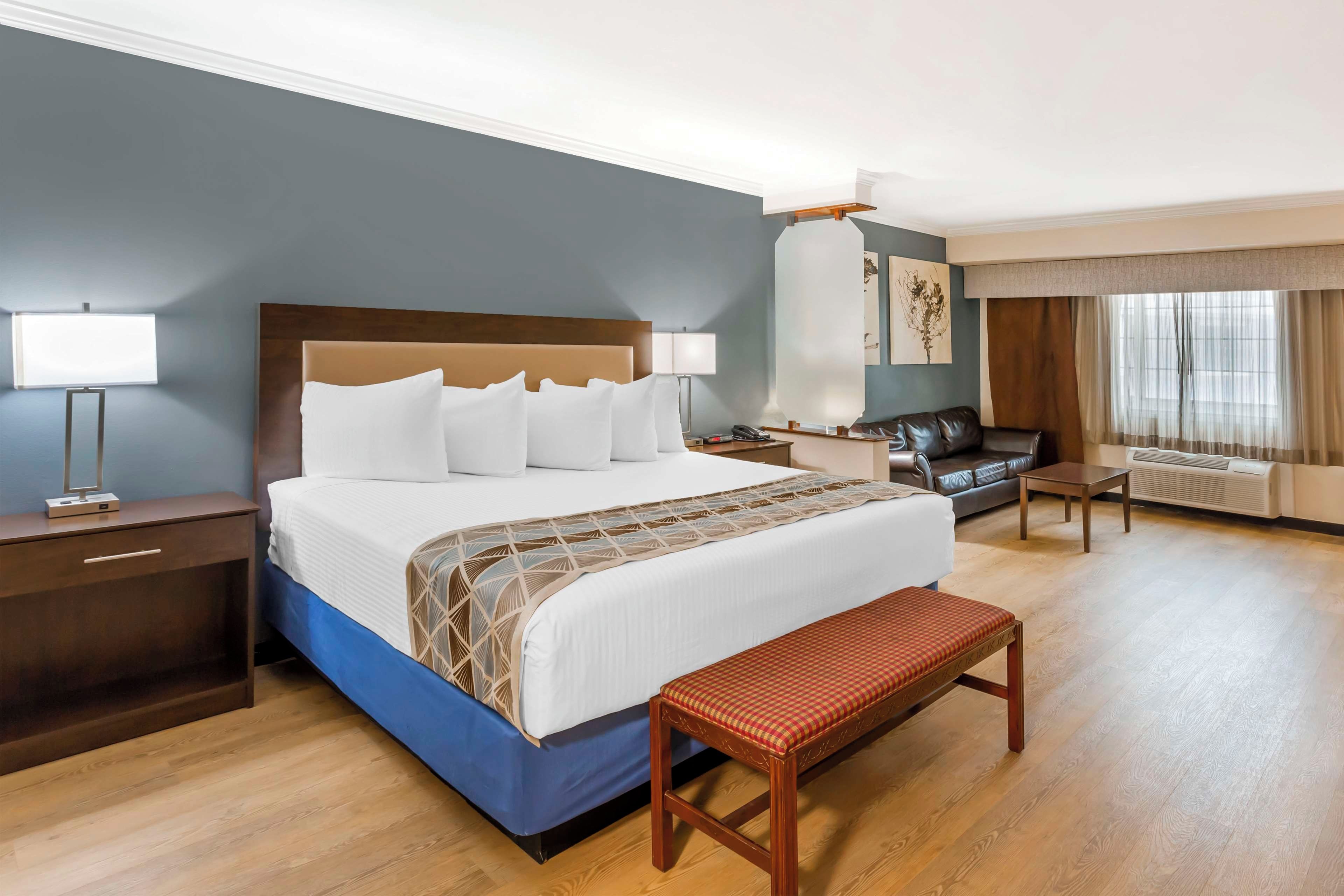 Una habitación de hotel con una cama grande, mesitas de noche, un escritorio, una silla, un banco y una ventana con cortinas.