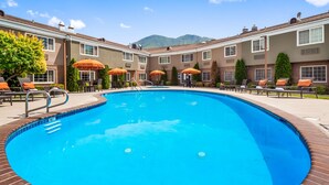 A swimming pool with lounge chairs and umbrellas, surrounded by a brick patio and a building with multiple windows. - Best Western Mountain View Inn (Springville)