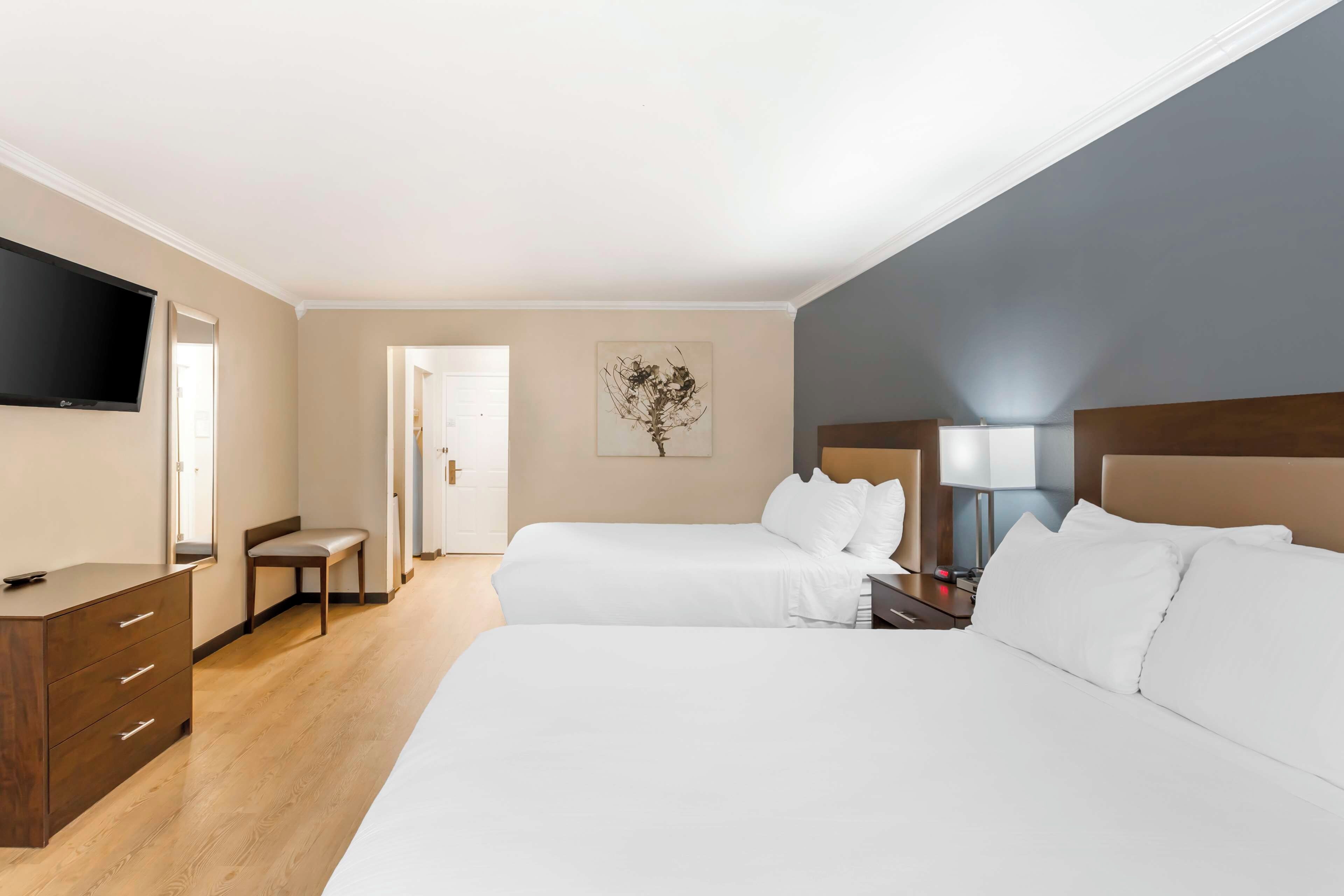 A hotel room with two beds, a desk, a chair, a flat-screen TV, and a painting on the wall.