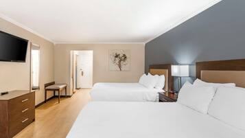 A hotel room with two beds, a desk, a chair, a flat-screen TV, and a painting on the wall.