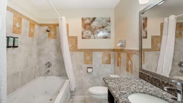 A bathroom with a bathtub, toilet, and sink, featuring a large mirror and decorative wall tiles.