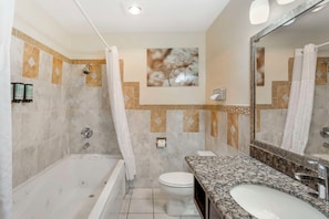 A bathroom with a bathtub, toilet, and sink, featuring a large mirror and decorative wall tiles.