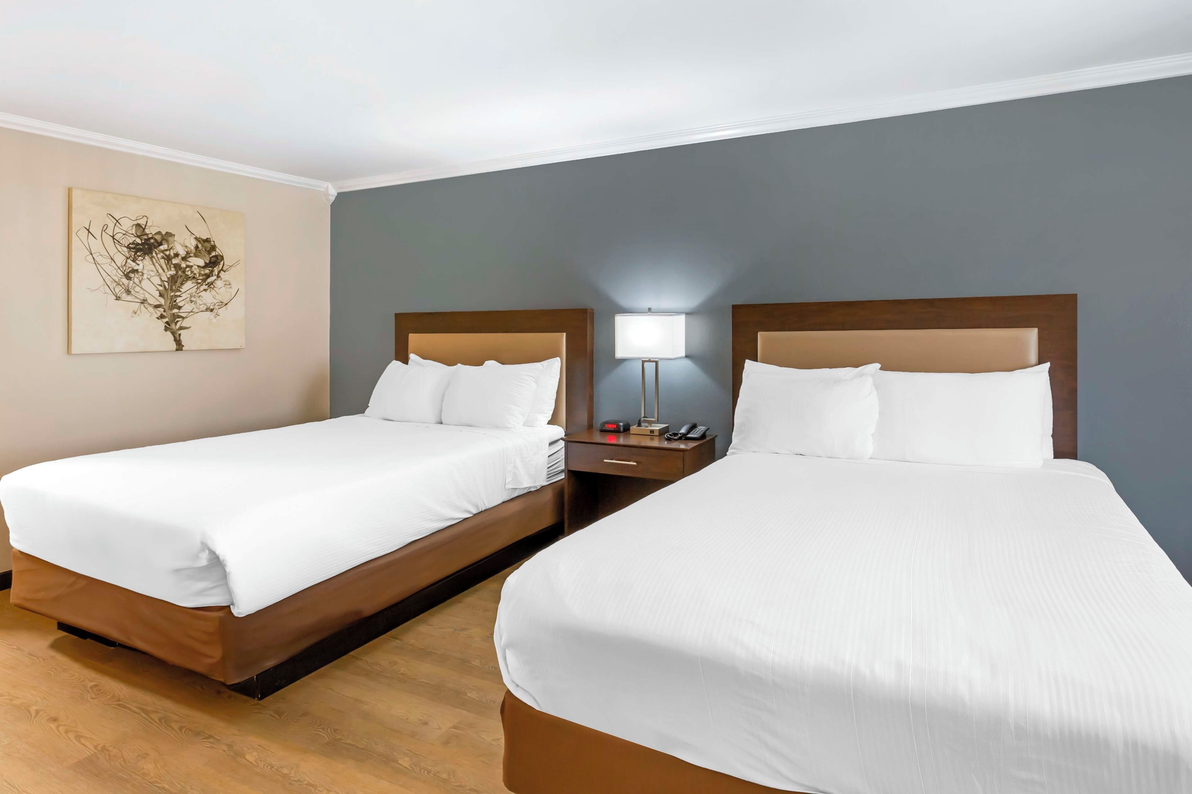 A hotel room with two single beds, a nightstand with a lamp, a clock, and a telephone.