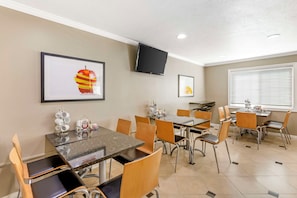 A hotel dining area with tables and chairs, a flat-screen TV mounted on the wall, and artwork on the walls.