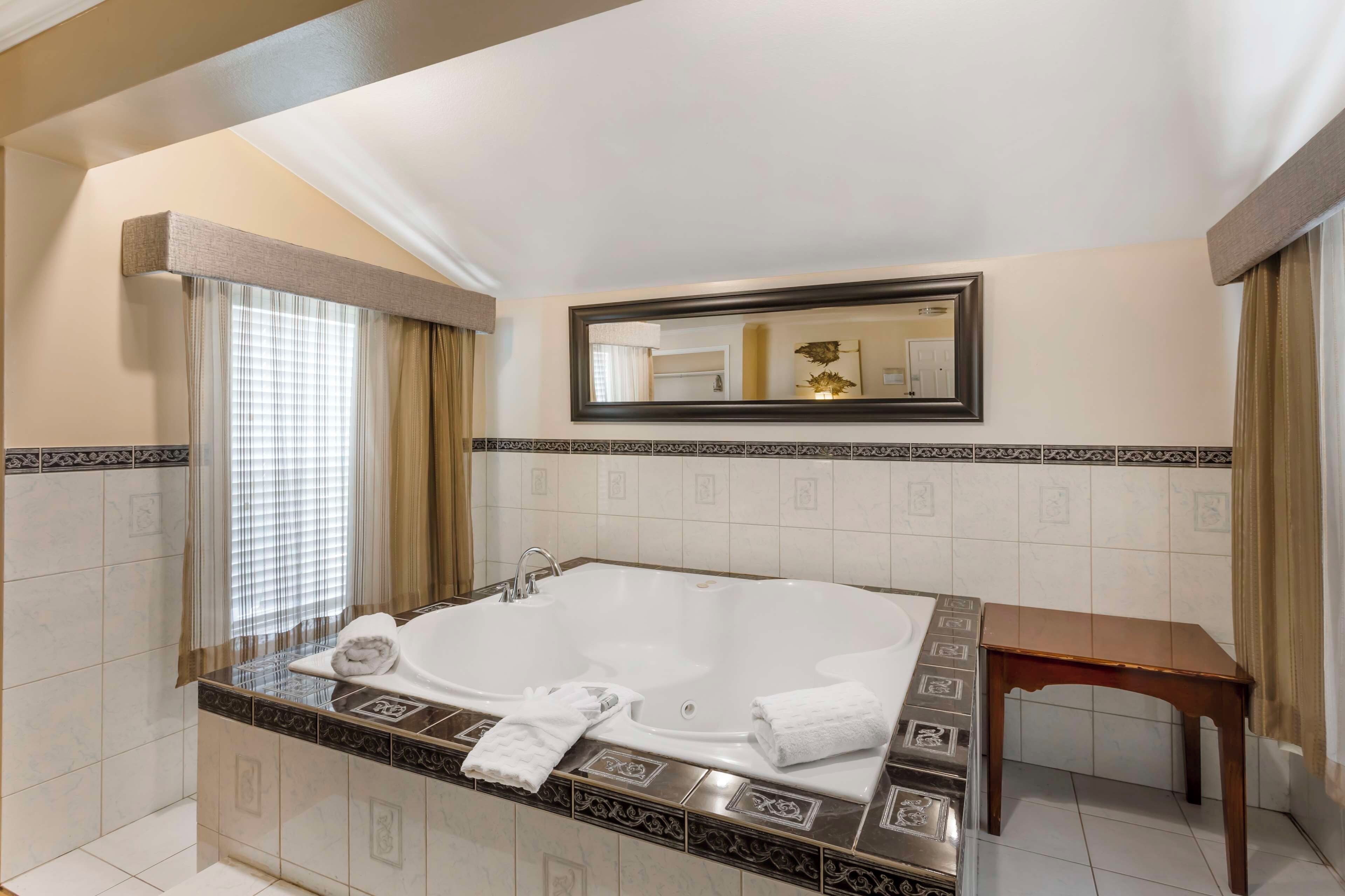 A bathroom with a large bathtub, a mirror, and a wooden bench.