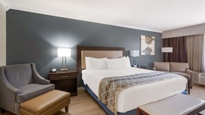 A hotel room with a large bed, two armchairs, a bench, a nightstand, and a lamp. - Best Western Mountain View Inn (Springville)