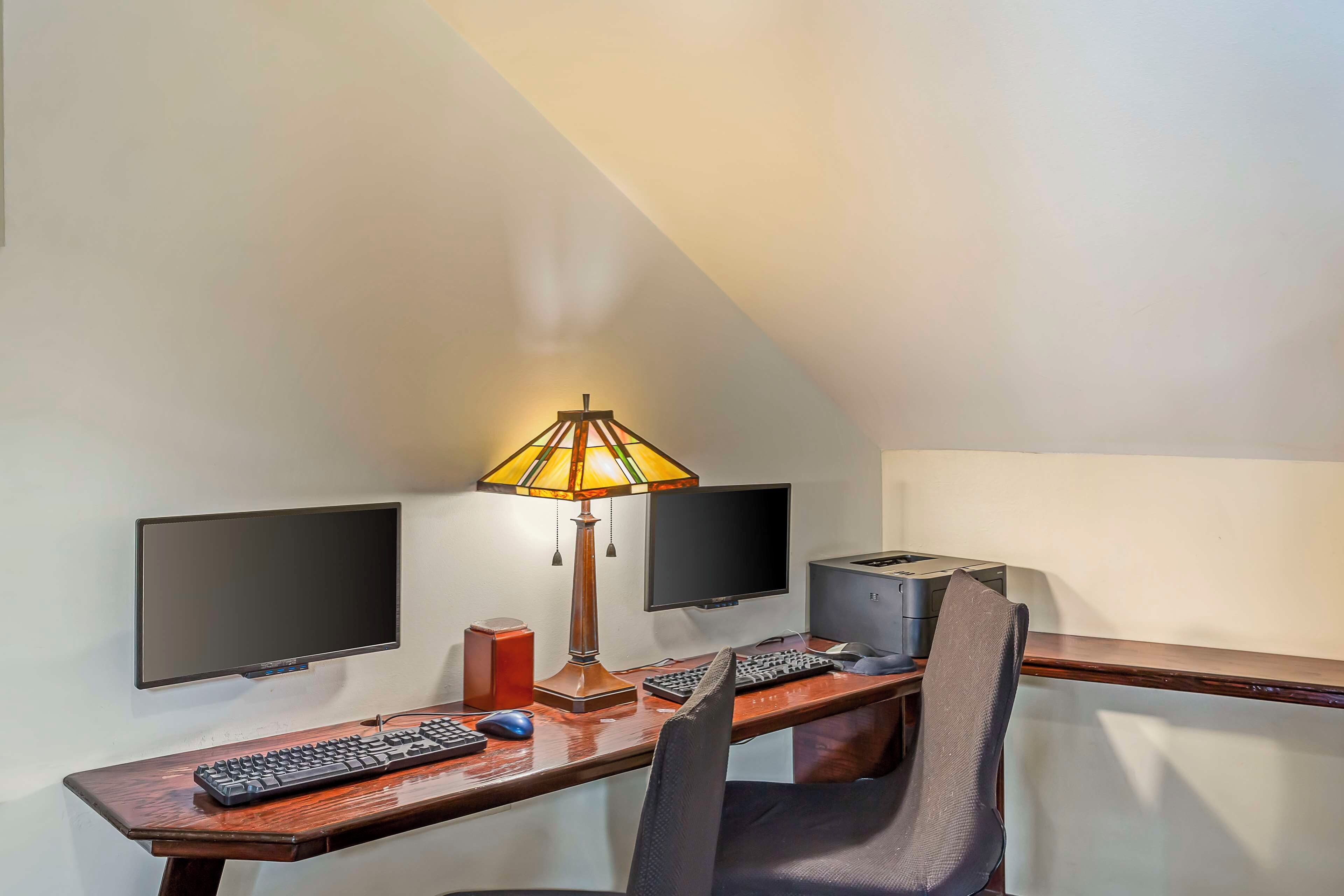 A small, private office with a desk, two monitors, a keyboard, a mouse, a lamp, and a printer.