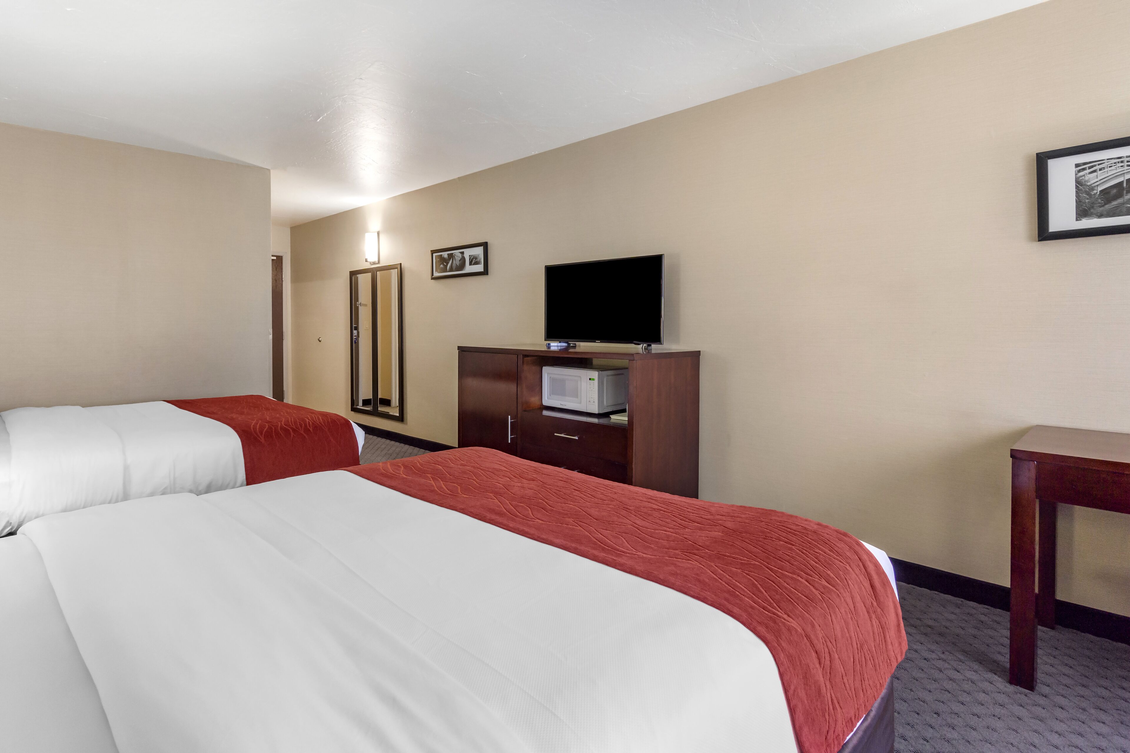 A hotel room with two beds, a television, a microwave, and a desk.