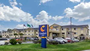 A Comfort Inn hotel with a parking lot and a clear blue sky with clouds.