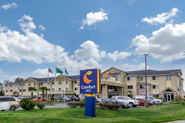 A Comfort Inn hotel with a parking lot and a clear blue sky with clouds.