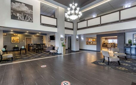 A spacious lobby with a high ceiling, a chandelier, seating areas, and a large painting of a cityscape.