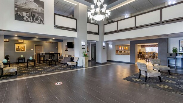 A spacious lobby with a high ceiling, a chandelier, seating areas, and a large painting of a cityscape.