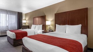 A hotel room with two beds, each with a red and white bedspread, a wooden headboard, and a nightstand with a lamp.