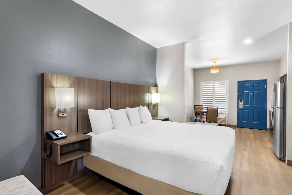 A hotel room with a large bed, bedside lamps, a phone, a desk with a chair, and a refrigerator.