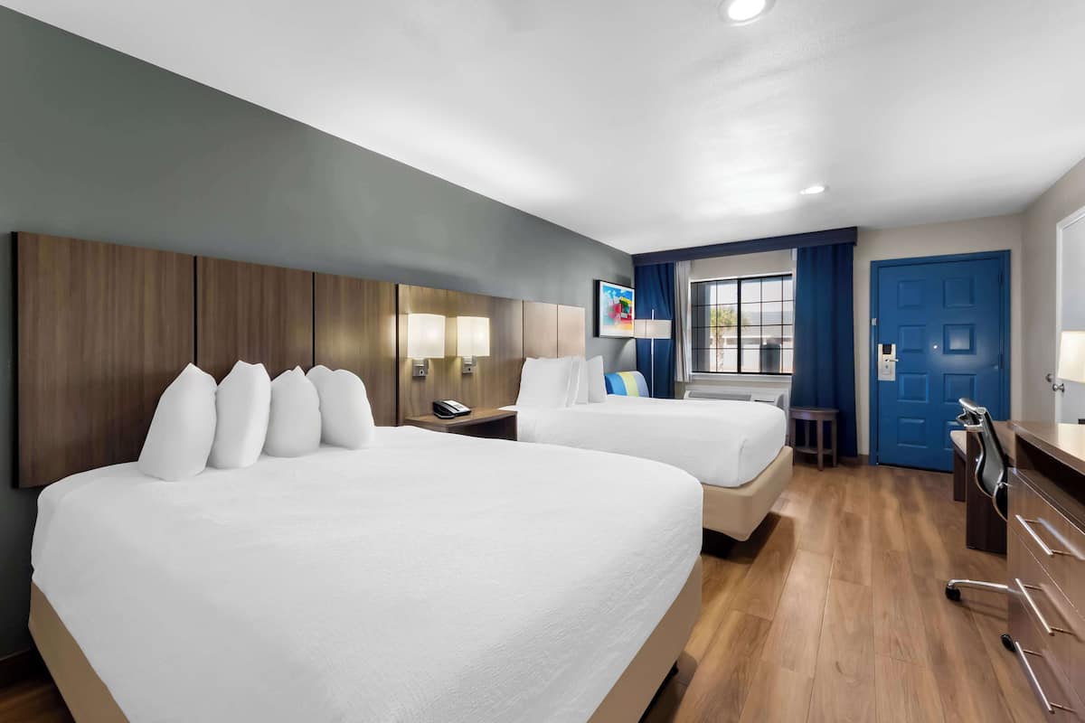 A hotel room with two beds, a desk, a chair, and a window with curtains.