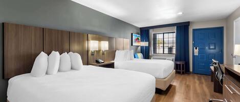 Habitación de hotel con dos camas, un escritorio, una silla y una ventana con cortinas.