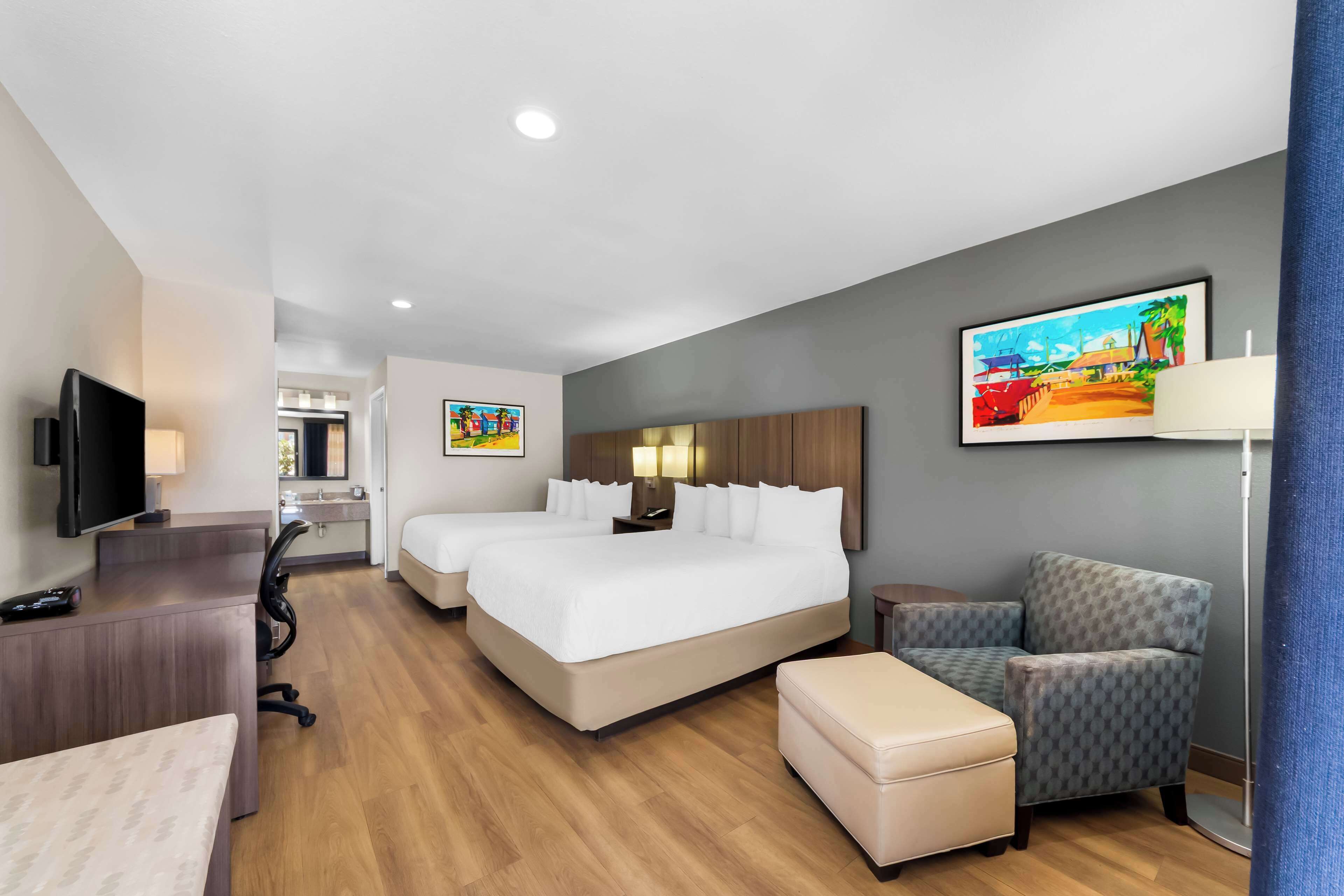 Een hotelkamer met een groot bed, een bureau, een stoel, een televisie en een schilderij aan de muur.