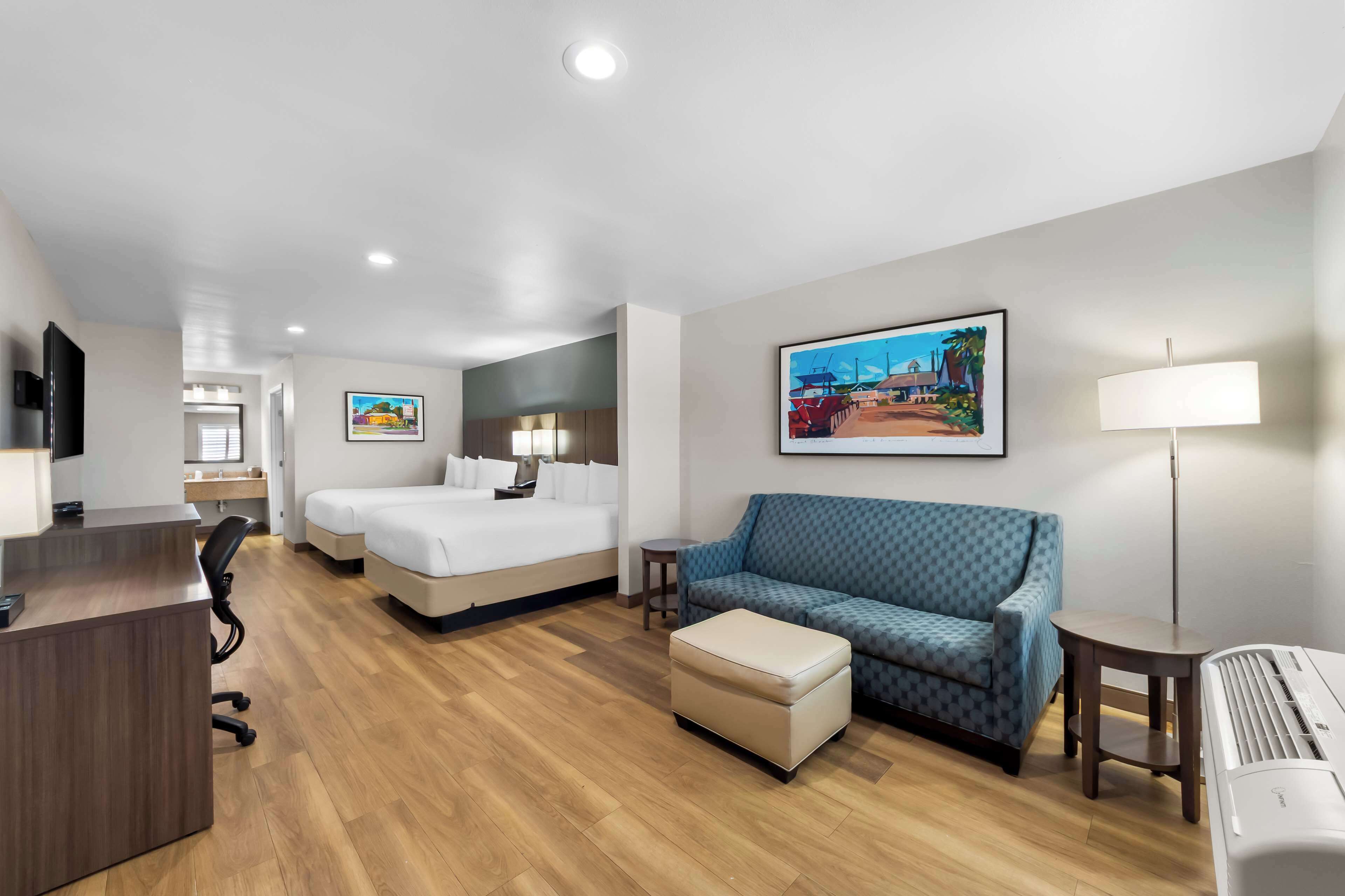 A hotel room with a bed, a sofa, a desk, and a lamp.