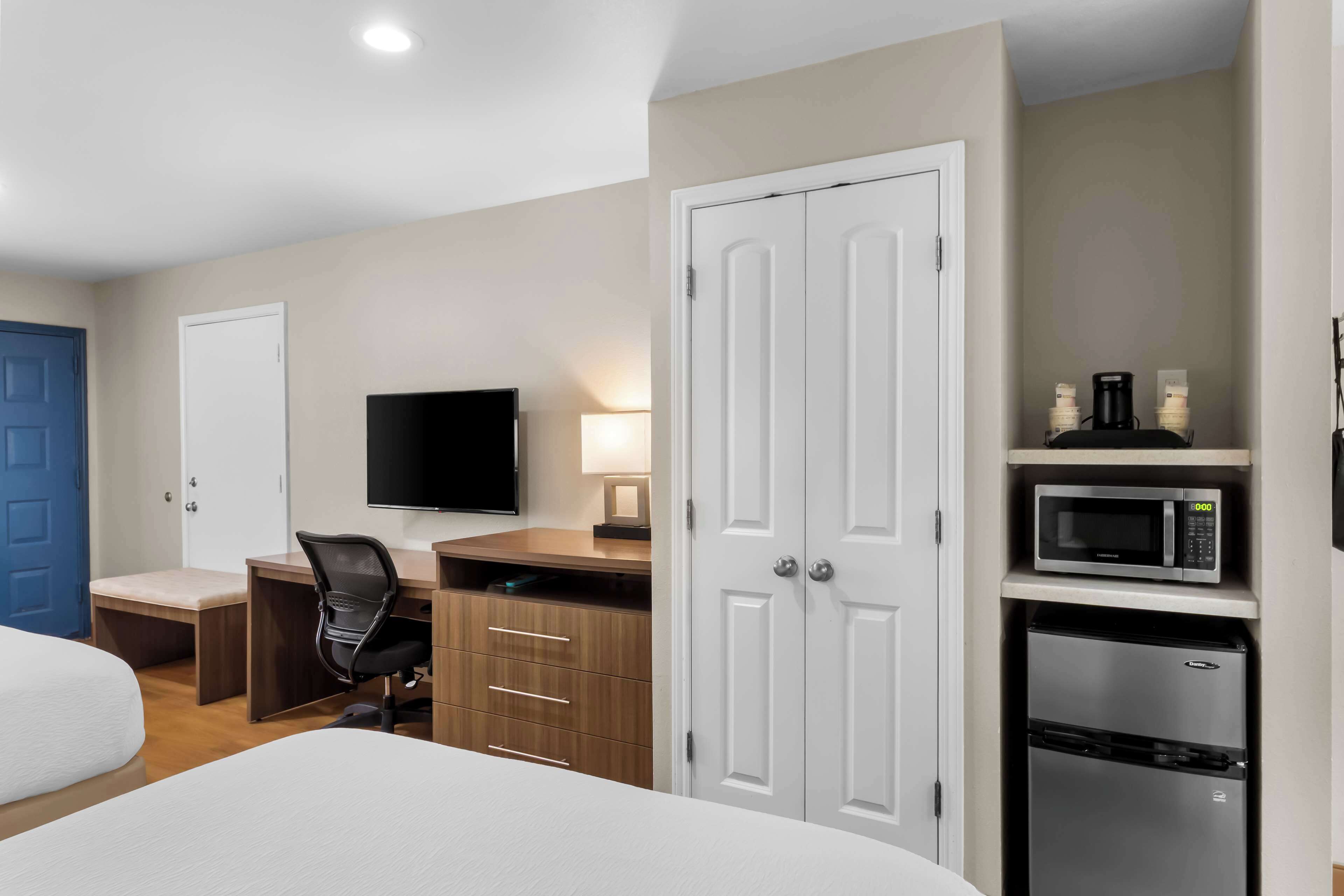 A hotel room with a bed, a desk with a computer, a TV, a wardrobe, a microwave, and a refrigerator.