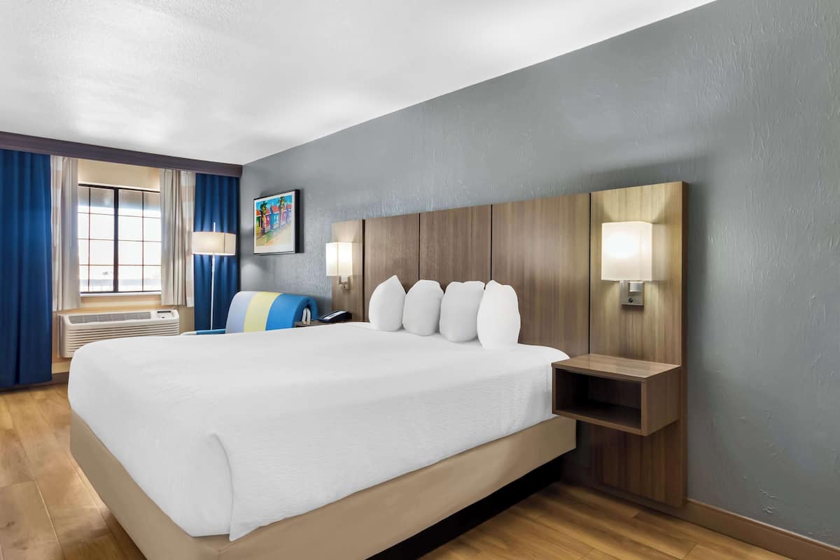 A hotel room with a large bed, wooden headboard, bedside lamps, and a window with curtains.