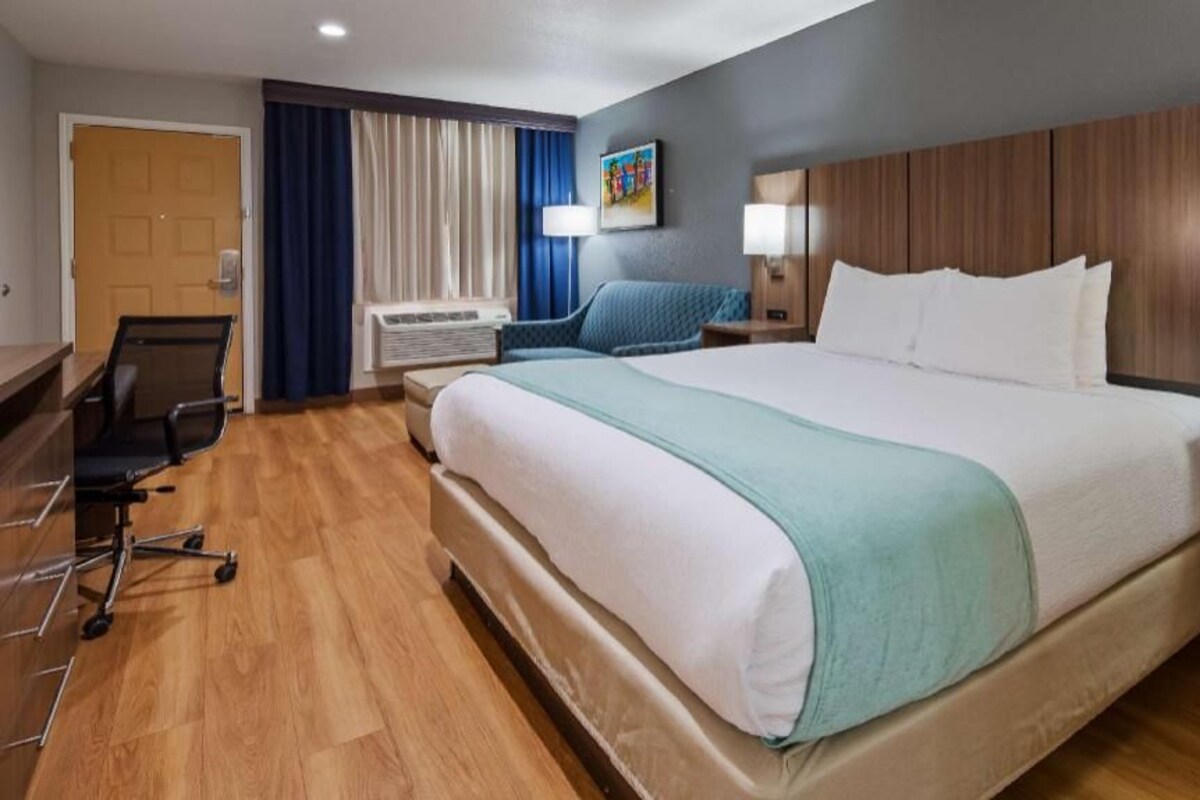 A hotel room with a large bed, a desk, a chair, a desk lamp, and a wall-mounted TV.