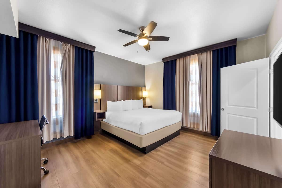 A hotel room with a bed, desk, and ceiling fan.
