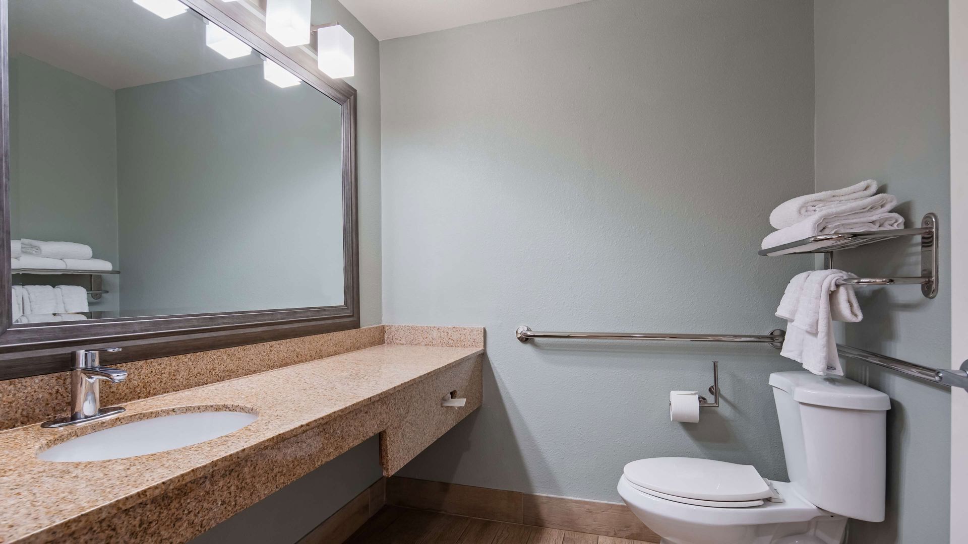 A bathroom with a granite countertop, a mirror, a toilet, and a towel rack.