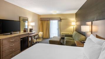 A hotel room with a large bed, a desk with a television, a chair, a sofa, and a lamp.