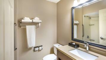 Une salle de bain moderne équipée de toilettes, d’un lavabo et d’un miroir. On y trouve également un porte-serviettes avec des serviettes pliées et un sèche-mains.