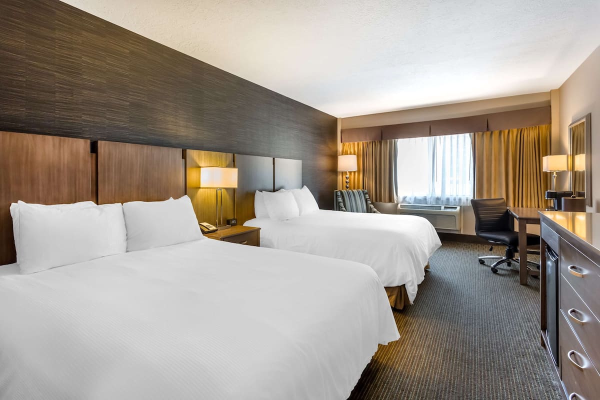 A hotel room with two beds, a desk, a chair, and a large window with curtains.