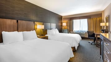 Een hotelkamer met twee bedden, een bureau, een stoel en een groot raam met gordijnen.