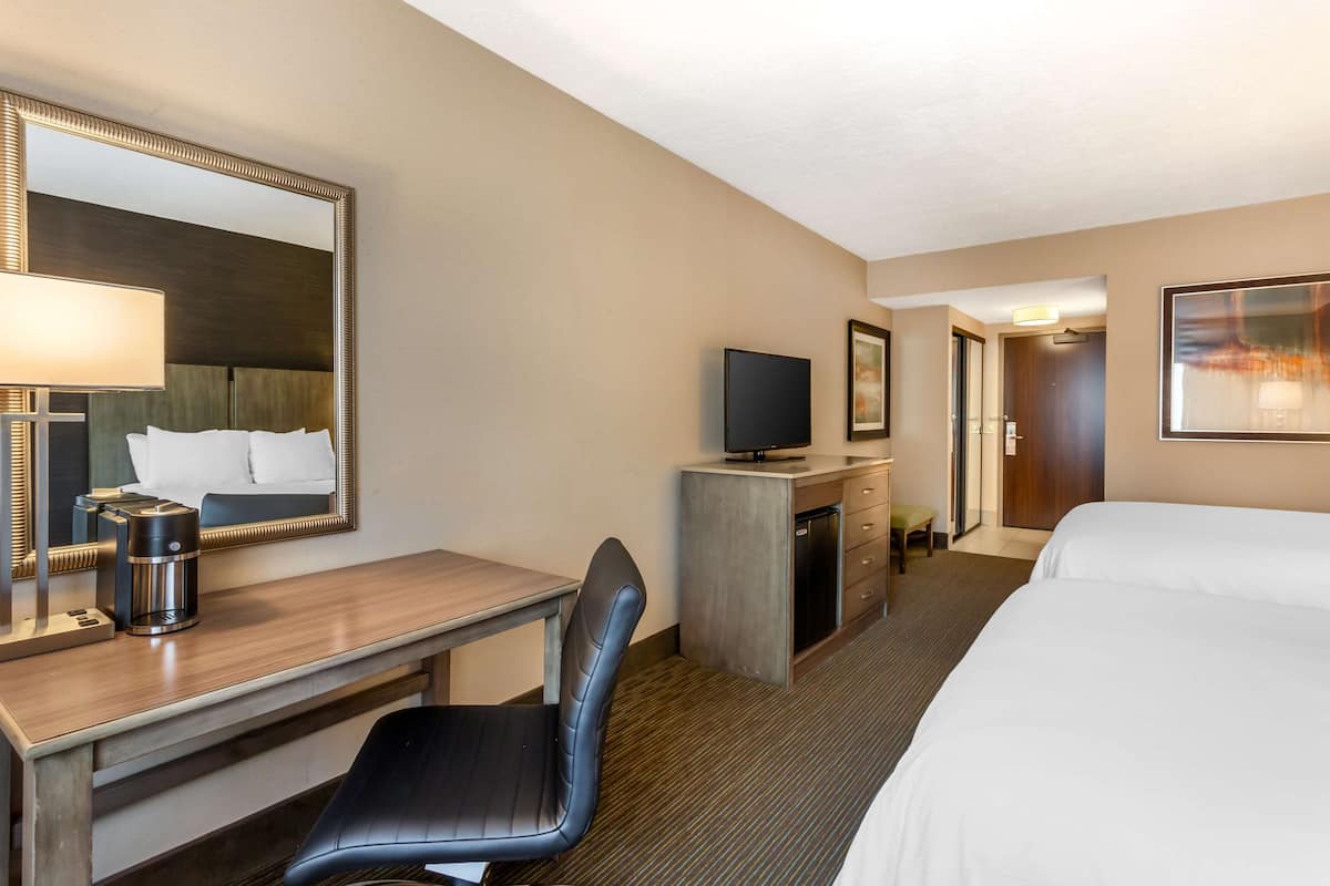 A hotel room with a bed, a desk with a chair, a television, a coffee maker, and a mirror.