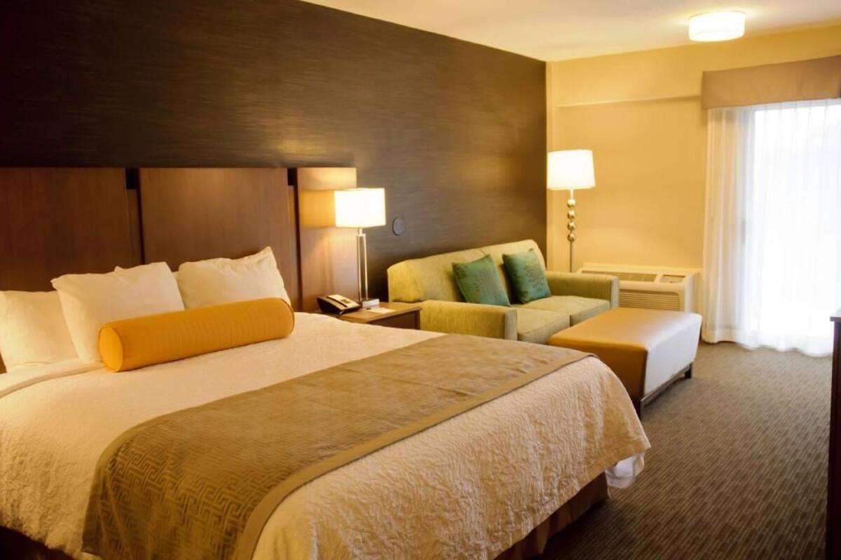 A hotel room with a large bed, a sofa, a desk, and a lamp.
