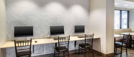 Un espacio de trabajo moderno con tres escritorios, cada uno con un monitor de ordenador y una silla. La habitación tiene un papel tapiz estampado y suelo de madera.
