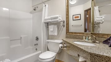 Un baño moderno con bañera, inodoro y lavamanos. Hay toallas ordenadas en un perchero y un espejo enmarco sobre el lavamanos.