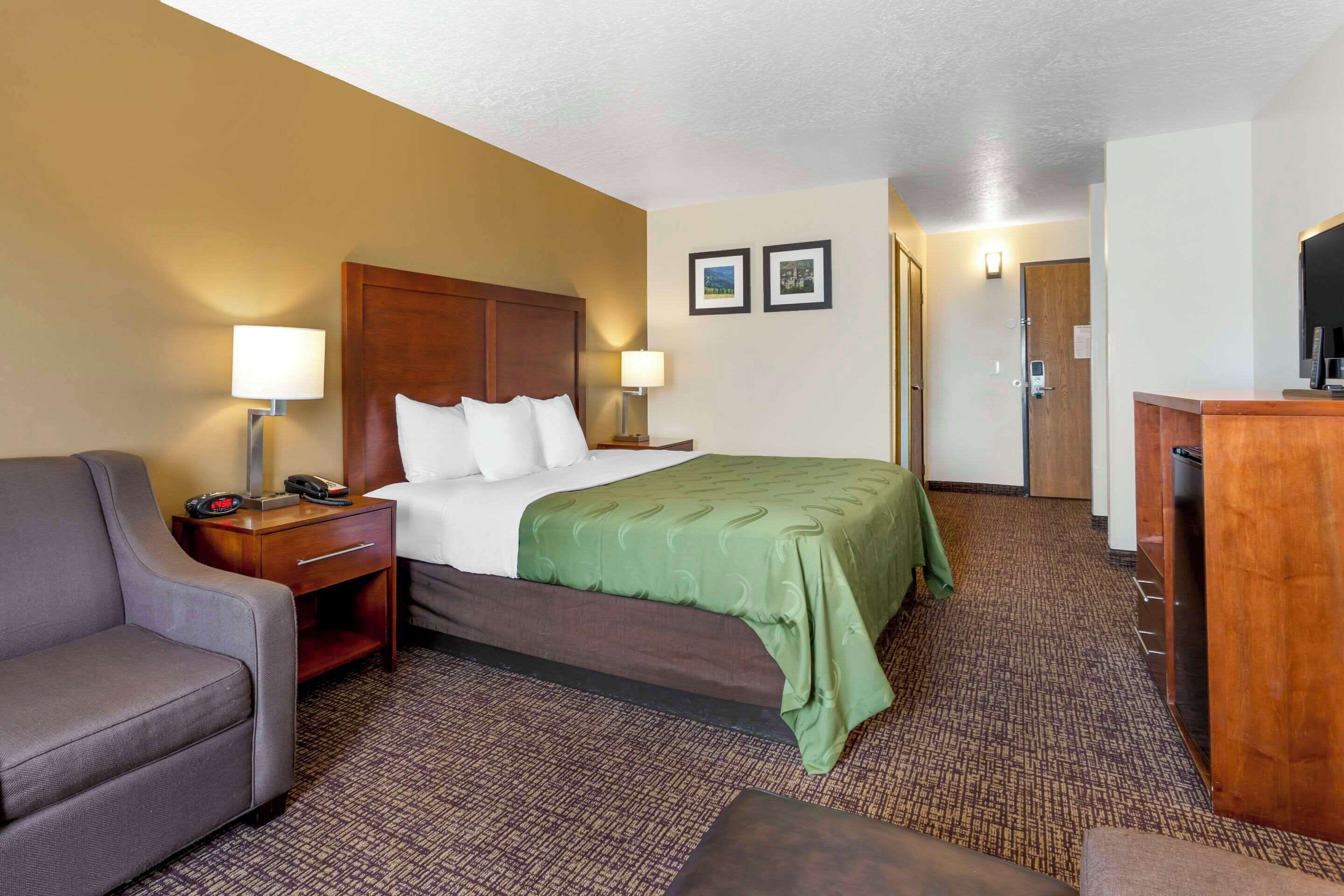 Una habitación de hotel con cama, escritorio con lámpara, silla y televisor.