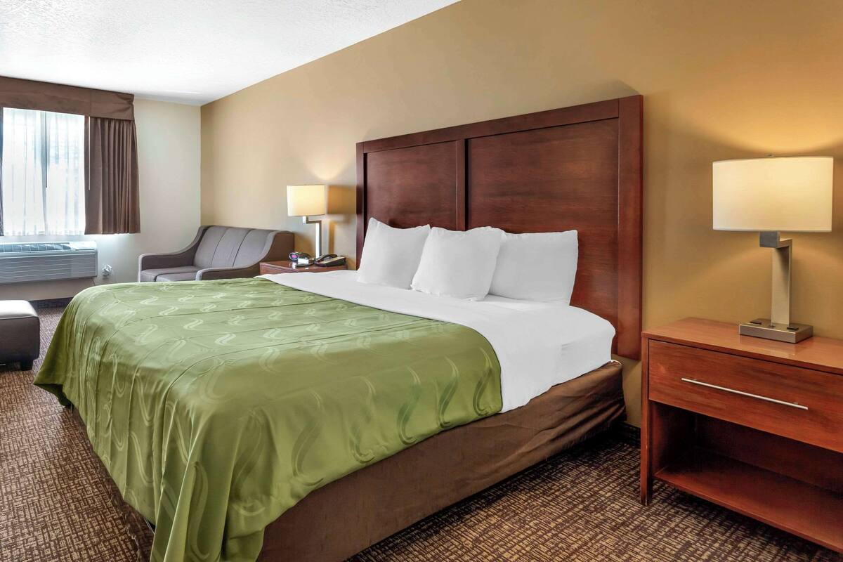 Ein Hotelzimmer mit einem großen Bett, einem Holz-Kopfteil, zwei Nachttischen mit Lampen, einem Sessel und einem Schreibtisch.