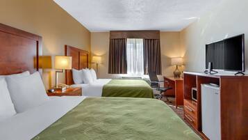 Een hotelkamer met twee bedden, een bureau met een computer, een televisie en een raam met gordijnen.