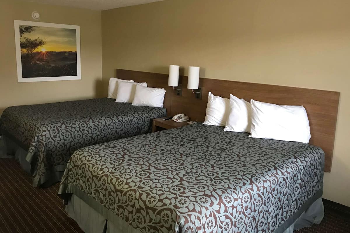 A hotel room with two beds, a nightstand, a phone, and a painting of a sunset on the wall.