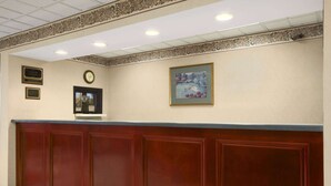 A reception area with a wooden reception desk, a clock, and framed artwork on the wall. - Days Inn By Wyndham Lexington/Columbia (Lexington)