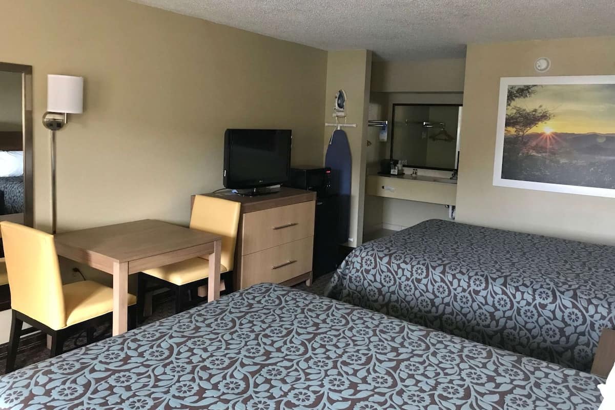 A hotel room with a desk, two beds, a television, a mirror, and a painting on the wall.