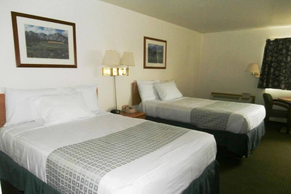 A hotel room with two beds, a desk, and two lamps.