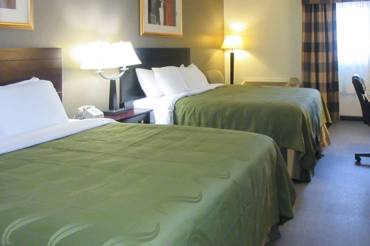 A hotel room with two beds, a desk with a lamp, a chair, and a telephone.