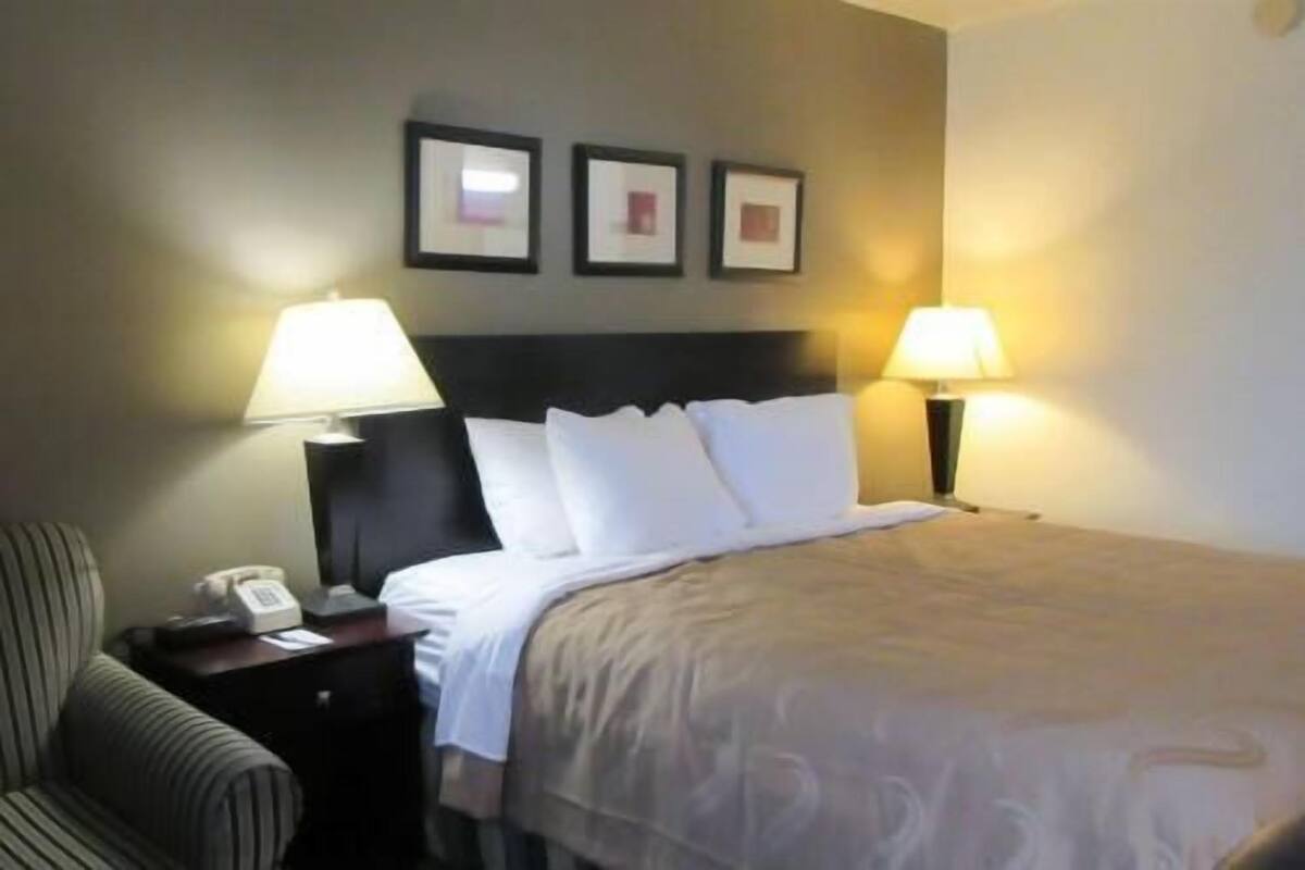 A hotel room with a bed, two bedside lamps, a chair, and a telephone on a nightstand.