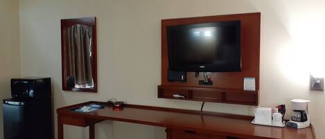 A hotel room with a wooden desk, a television mounted on the wall, a microwave, and a coffee maker.