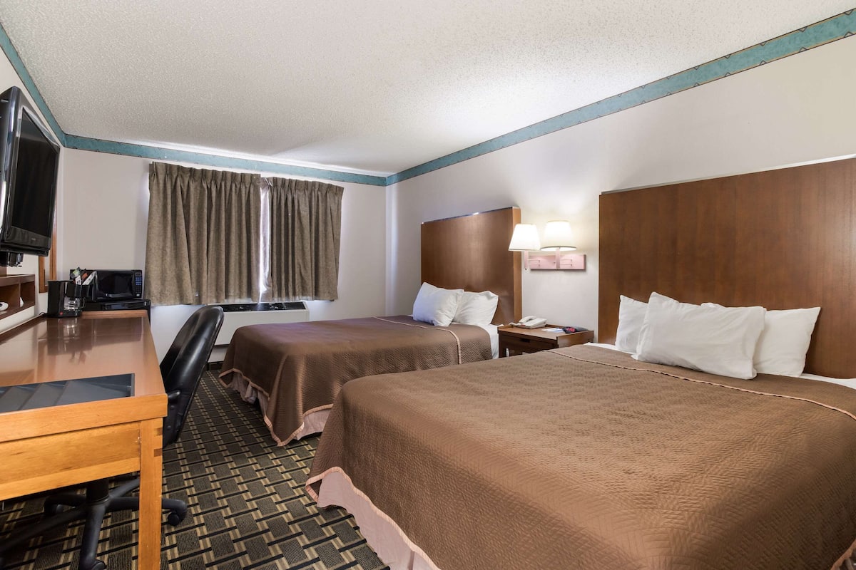 A hotel room with two beds, a desk with a chair, a television, a microwave, and a window with curtains.