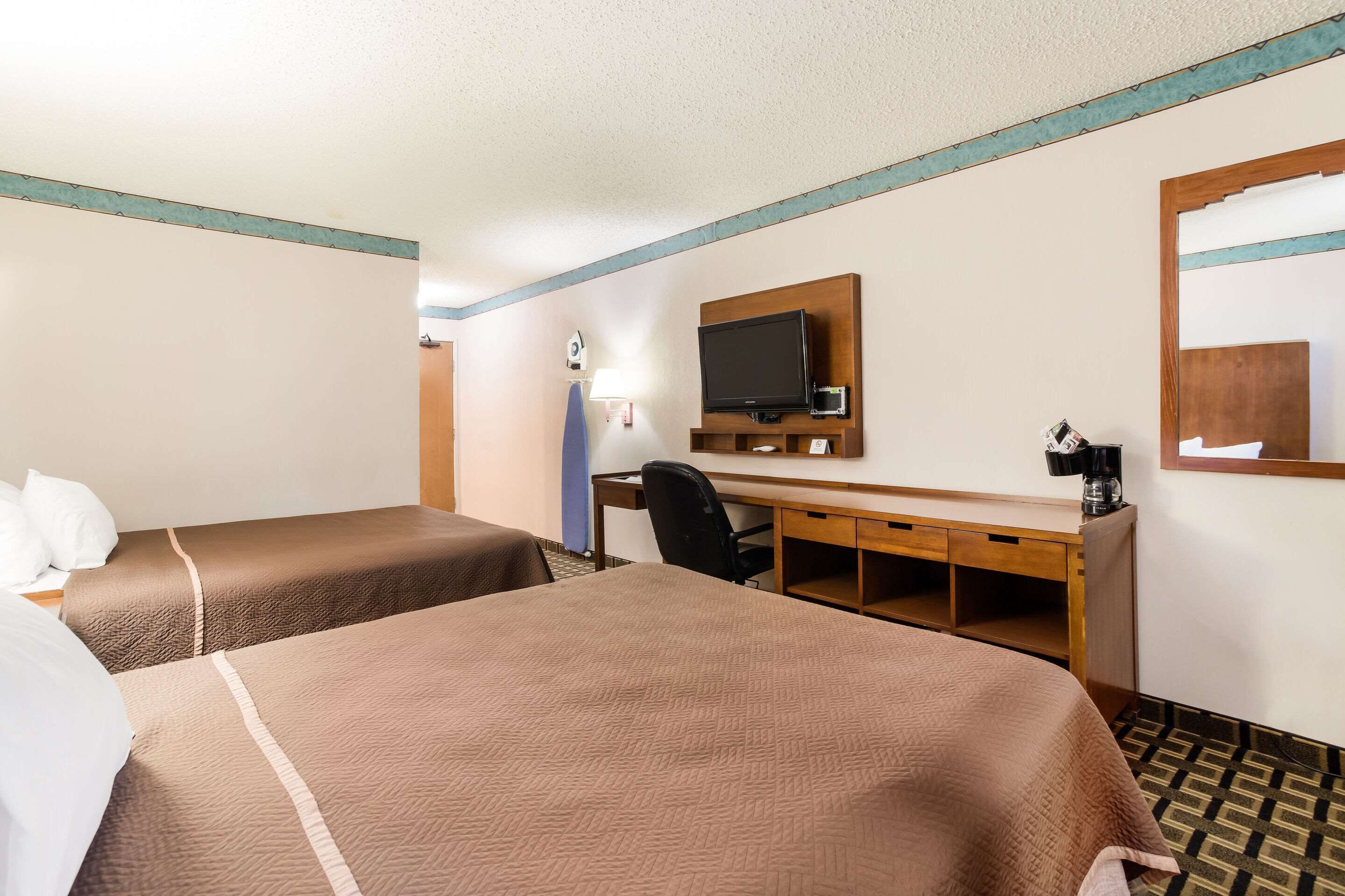 A hotel room with two beds, a desk, a chair, a television, and a coffee maker.